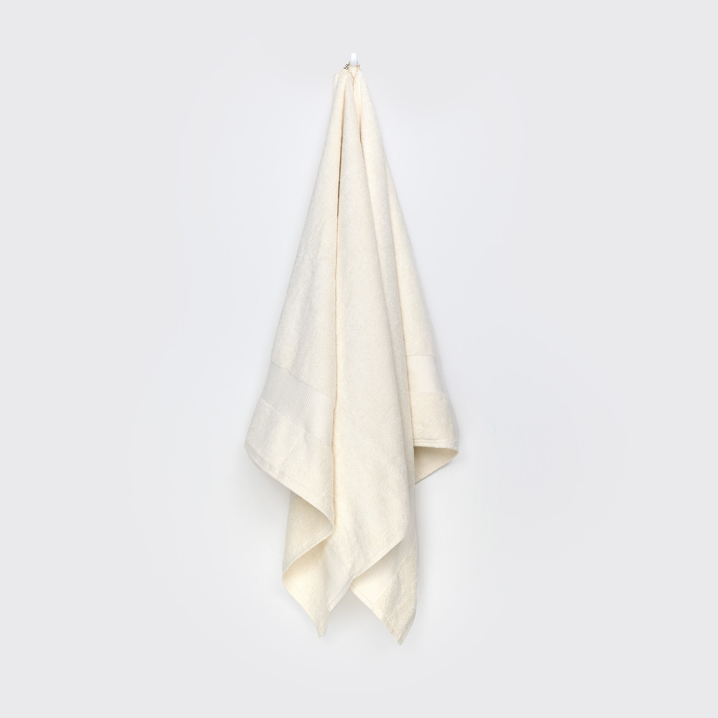 organic-cotton-bath-towel-in-natural-colour-hanging-on-a-wall-by-sojao