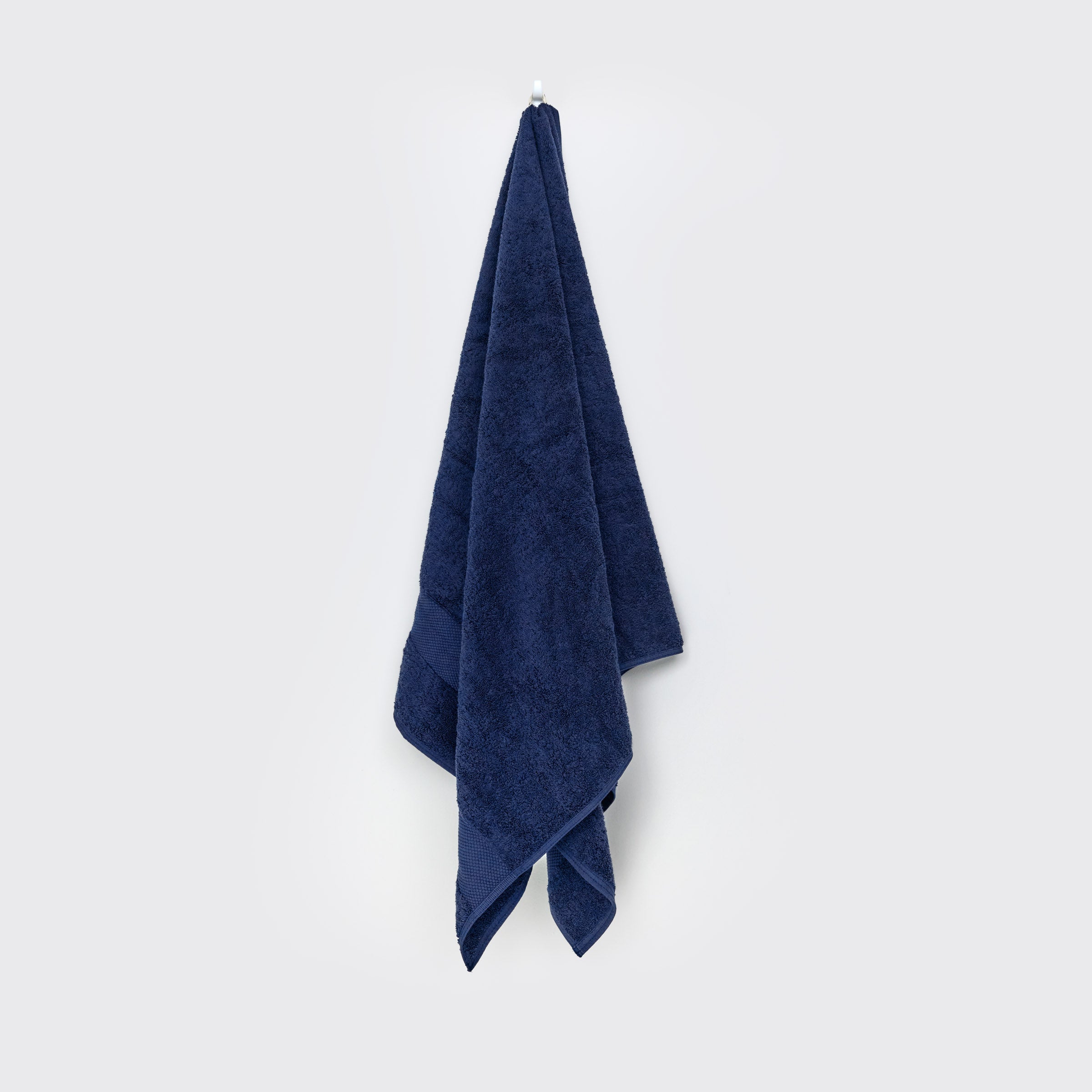 organic-cotton-bath-towel-in-navy-colour-hanging-on-a-wall-by-sojao