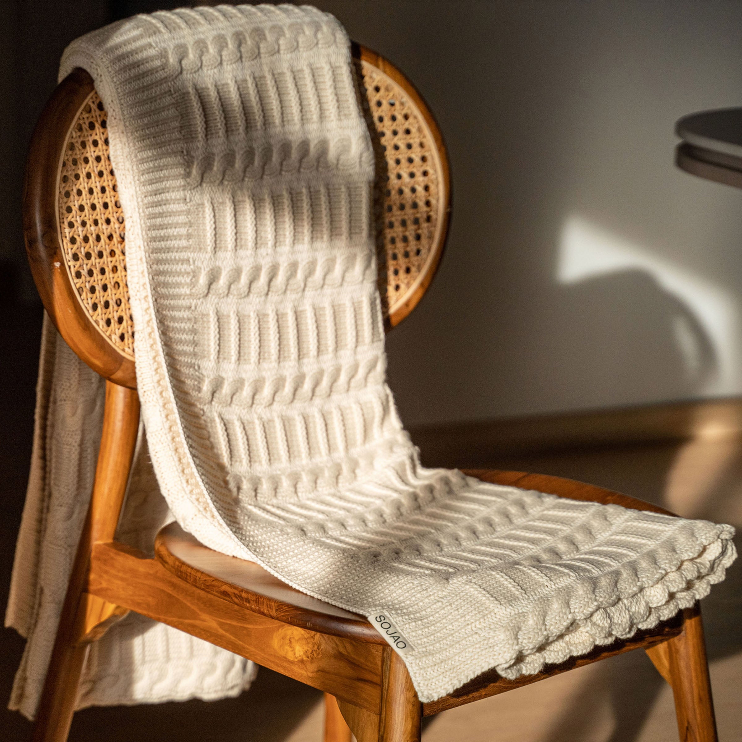 organic-cotton-cable-knit-throw-in-ivory-colour-hanging-over-a-wooden-chair-by-sojao